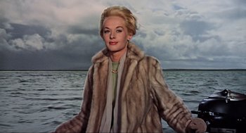 Movie still from “The Birds” (1963), directed by Alfred Hitchcock – A painting of a woman in fur standing in front of a body of water; Medium shot, Low angle