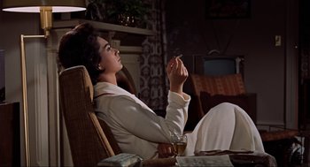 Movie still from “The Birds” (1963), directed by Alfred Hitchcock – A woman sitting in a chair with a cigarette in her mouth; Medium shot, Low angle