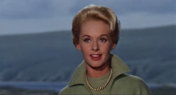 Movie still from “The Birds” (1963), directed by Alfred Hitchcock – An older woman wearing a green jacket and a gold necklace; Close Up shot, Low angle