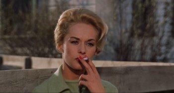 Movie still from “The Birds” (1963), directed by Alfred Hitchcock – A woman smoking a cigarette while sitting on a bench; Close Up shot, Low angle