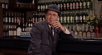 Movie still from “The Birds” (1963), directed by Alfred Hitchcock – A man sitting at a bar with a drink in his hand; Medium shot, Low angle