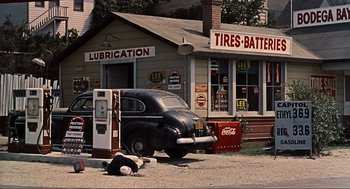 Movie still from “The Birds” (1963), directed by Alfred Hitchcock – An old time gas station with an old car parked in front of it; Extreme Wide shot, High angle
