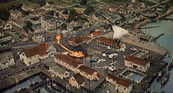 Movie still from “The Birds” (1963), directed by Alfred Hitchcock – An aerial view of a town with a fire in the middle of the street; Extreme Wide shot, High angle