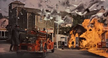 Movie still from “The Birds” (1963), directed by Alfred Hitchcock – An old fire truck in front of a burning building; Wide shot, Low angle