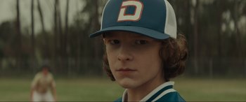 Movie still from “The Black Phone” (2021), directed by Scott Derrickson – A young boy wearing a baseball uniform and hat; Close Up shot, Over the shoulder angle