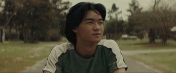 Movie still from “The Black Phone” (2021), directed by Scott Derrickson – A young man sitting in the grass looking up; Close Up shot, Over the shoulder angle