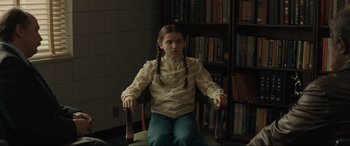 Movie still from “The Black Phone” (2021), directed by Scott Derrickson – A young girl sitting in a chair in a library; Medium shot, Over the shoulder angle