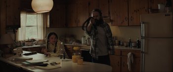 Movie still from “The Black Phone” (2021), directed by Scott Derrickson – A man with a long beard is holding a hula hoop in a kitchen; Medium shot, Over the shoulder angle