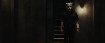 Movie still from “The Black Phone” (2021), directed by Scott Derrickson – A man wearing a demon mask standing in front of stairs; Medium shot, Low angle
