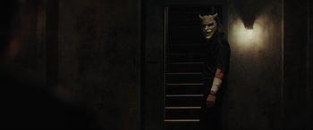 Movie still from “The Black Phone” (2021), directed by Scott Derrickson – A person with a mask on standing in front of some stairs; Medium shot, Low angle