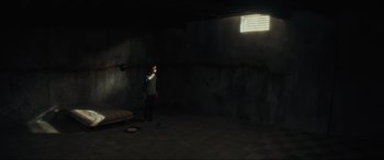 Movie still from “The Black Phone” (2021), directed by Scott Derrickson – A man standing in a dark room holding a cell phone; Wide shot, High angle