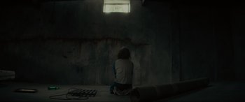 Movie still from “The Black Phone” (2021), directed by Scott Derrickson – A person sitting on the ground in a dark room; Wide shot, High angle