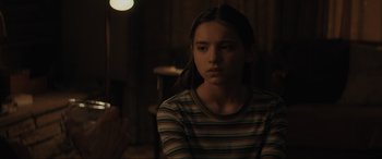 Movie still from “The Black Phone” (2021), directed by Scott Derrickson – A young girl in a striped shirt is sitting in a dark room; Close Up shot, Over the shoulder angle