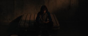Movie still from “The Black Phone” (2021), directed by Scott Derrickson – A man sitting on a couch in a dark room; Medium shot, High angle