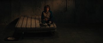 Movie still from “The Black Phone” (2021), directed by Scott Derrickson – A person sitting on a mattress in a room; Wide shot, High angle