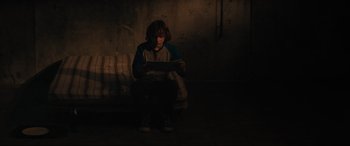 Movie still from “The Black Phone” (2021), directed by Scott Derrickson – A person sitting in a dark room holding a tablet; Wide shot, High angle