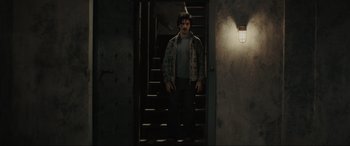 Movie still from “The Black Phone” (2021), directed by Scott Derrickson – A man standing on a set of stairs in a dark room; Wide shot, Low angle