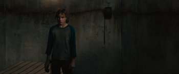 Movie still from “The Black Phone” (2021), directed by Scott Derrickson – A young boy standing in a dark room; Medium shot, Over the shoulder angle