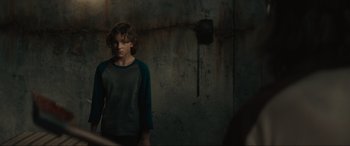 Movie still from “The Black Phone” (2021), directed by Scott Derrickson – A young man standing in a room with a wall behind him; Medium shot, Over the shoulder angle