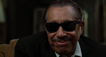 Movie still from “The Blues Brothers” (1980), directed by John Landis – An older man wearing a black suit and sunglasses; Close Up shot, Low angle