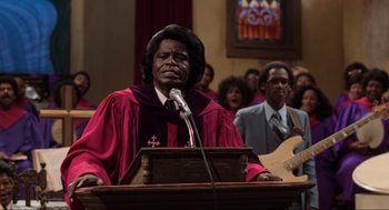Movie still from “The Blues Brothers” (1980), directed by John Landis – A man is speaking at a podium in front of a group of people; Medium shot, Low angle