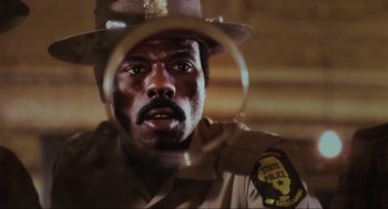 Movie still from “The Blues Brothers” (1980), directed by John Landis – A man in a police uniform looking at the camera; Close Up shot, Low angle