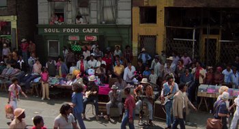 Movie still from “The Blues Brothers” (1980), directed by John Landis – A group of people sitting on the side of the street; Extreme Wide shot, High angle