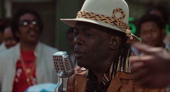 Movie still from “The Blues Brothers” (1980), directed by John Landis – An older man wearing a hat is singing into a microphone; Close Up shot, Low angle