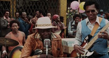 Movie still from “The Blues Brothers” (1980), directed by John Landis – An older man wearing a hat is holding a microphone; Medium shot, Low angle