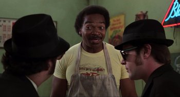 Movie still from “The Blues Brothers” (1980), directed by John Landis – A man in a yellow shirt and two other men in a black hat; Close Up shot, Over the shoulder angle