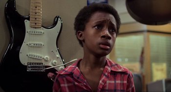 Movie still from “The Blues Brothers” (1980), directed by John Landis – A young boy in a plaid shirt is looking at the camera; Close Up shot, Over the shoulder angle