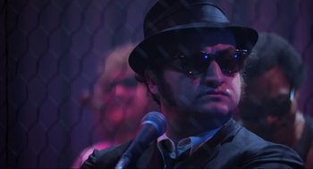 Movie still from “The Blues Brothers” (1980), directed by John Landis – A man wearing a hat and sunglasses holding a microphone; Close Up shot, Low angle