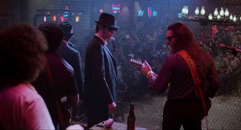 Movie still from “The Blues Brothers” (1980), directed by John Landis – A group of people in a room with a guitar; Wide shot, Over the shoulder angle