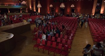 Movie still from “The Blues Brothers” (1980), directed by John Landis – People are sitting in rows of red chairs in an auditorium; Extreme Wide shot, High angle