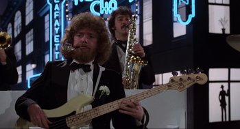 Movie still from “The Blues Brothers” (1980), directed by John Landis – A man in a tuxedo holding a guitar and a saxophone; Medium shot, Low angle