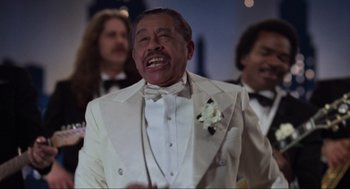 Movie still from “The Blues Brothers” (1980), directed by John Landis – An older man wearing a white tuxedo with a white flower in his lapel; Medium shot, Low angle