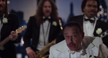 Movie still from “The Blues Brothers” (1980), directed by John Landis – A man in a white suit with a saxophone in front of him and another man in a black suit with a white bow tie; Medium shot, Low angle