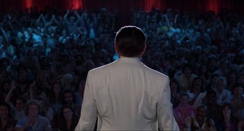 Movie still from “The Blues Brothers” (1980), directed by John Landis – A man in a white suit standing in front of an audience; Wide shot, Over the shoulder angle