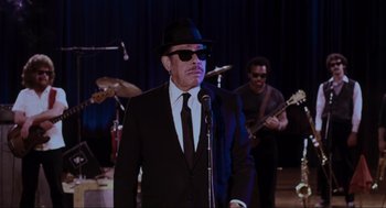 Movie still from “The Blues Brothers” (1980), directed by John Landis – A man wearing a suit and tie with a hat and sunglasses; Medium shot, Low angle