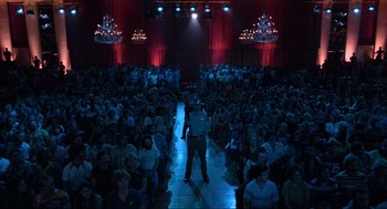 Movie still from “The Blues Brothers” (1980), directed by John Landis – A crowd of people sitting and standing in front of a stage; Extreme Wide shot, High angle