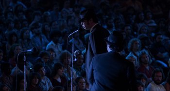 Movie still from “The Blues Brothers” (1980), directed by John Landis – A man in a suit and hat speaking to a crowd; Medium shot, High angle