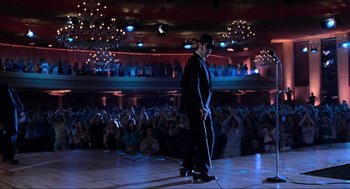 Movie still from “The Blues Brothers” (1980), directed by John Landis – A man in a black suit and hat on a stage; Wide shot, Low angle
