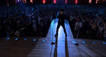 Movie still from “The Blues Brothers” (1980), directed by John Landis – A man standing on a stage in front of an audience; Wide shot, High angle