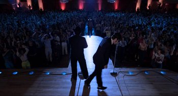 Movie still from “The Blues Brothers” (1980), directed by John Landis – A couple of men standing next to each other on a stage with microphones; Wide shot, Low angle