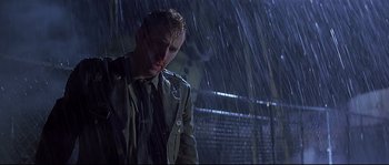 Movie still from “Con Air” (1997), directed by Simon West – A man standing in the pouring rain looking down; Medium shot, Low angle