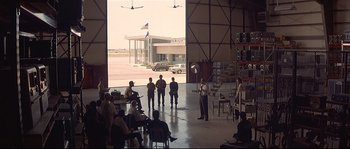 Movie still from “Con Air” (1997), directed by Simon West – A group of people standing in front of an airplane hangar; Extreme Wide shot, Over the shoulder angle
