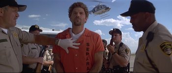 Movie still from “Con Air” (1997), directed by Simon West – A man in an orange prison uniform with his hand on his chest; Medium shot, Low angle