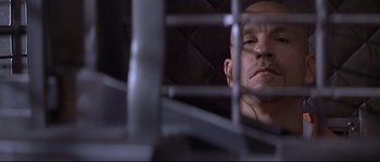 Movie still from “Con Air” (1997), directed by Simon West – A man with a shaved head looking through a cage; Close Up shot, Low angle