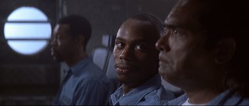 Movie still from “Con Air” (1997), directed by Simon West – Three men are standing in a room and one is looking at the camera; Close Up shot, Over the shoulder angle