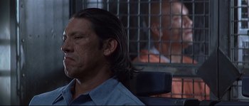 Movie still from “Con Air” (1997), directed by Simon West – A man with long hair sitting in a jail cell; Close Up shot, Over the shoulder angle